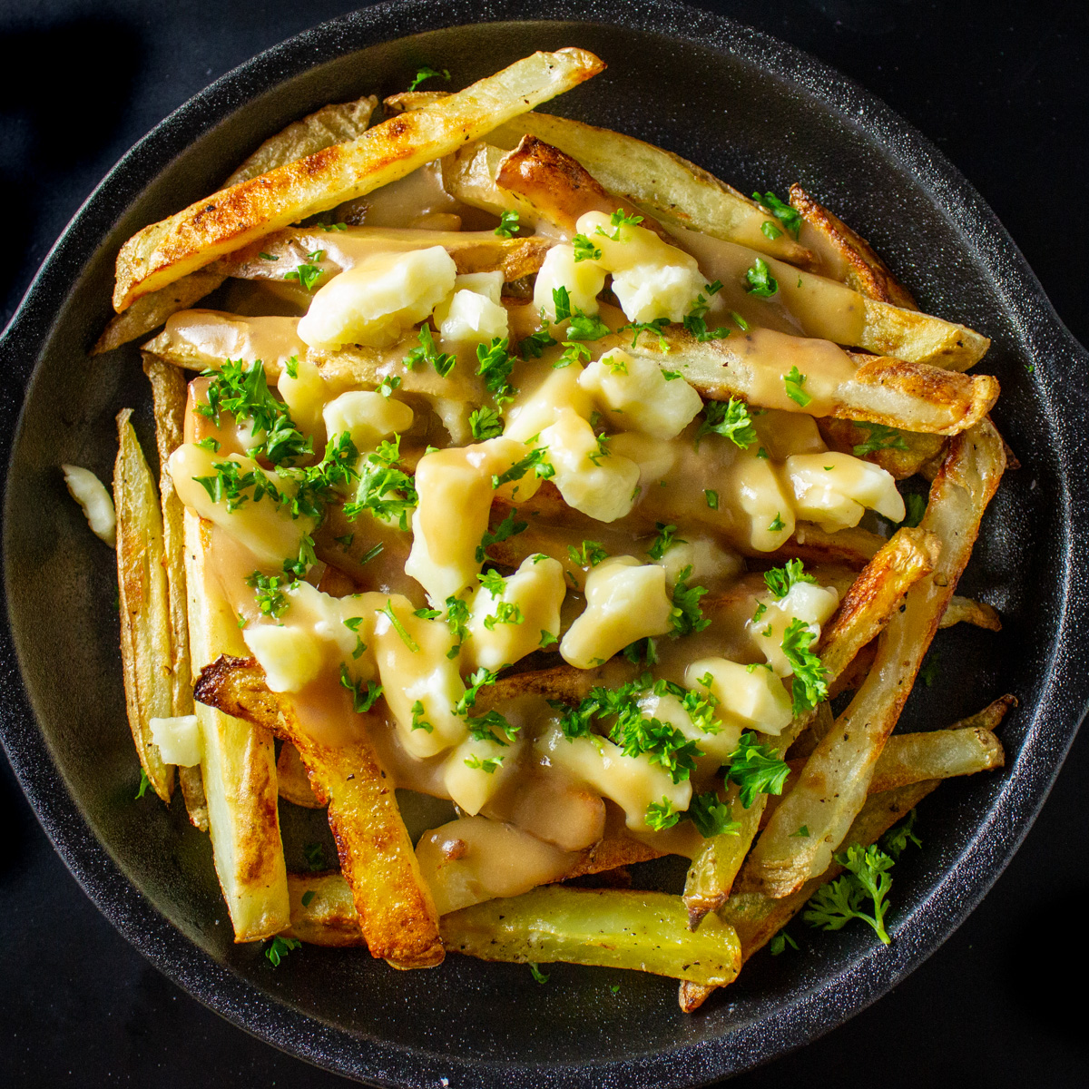 poutine on black plate sprinkled with parsley.