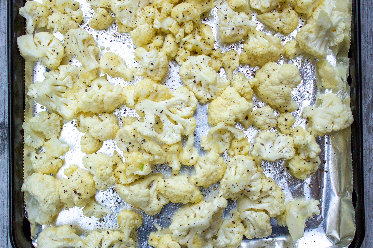 coated cauliflower laid out on lined baking sheet