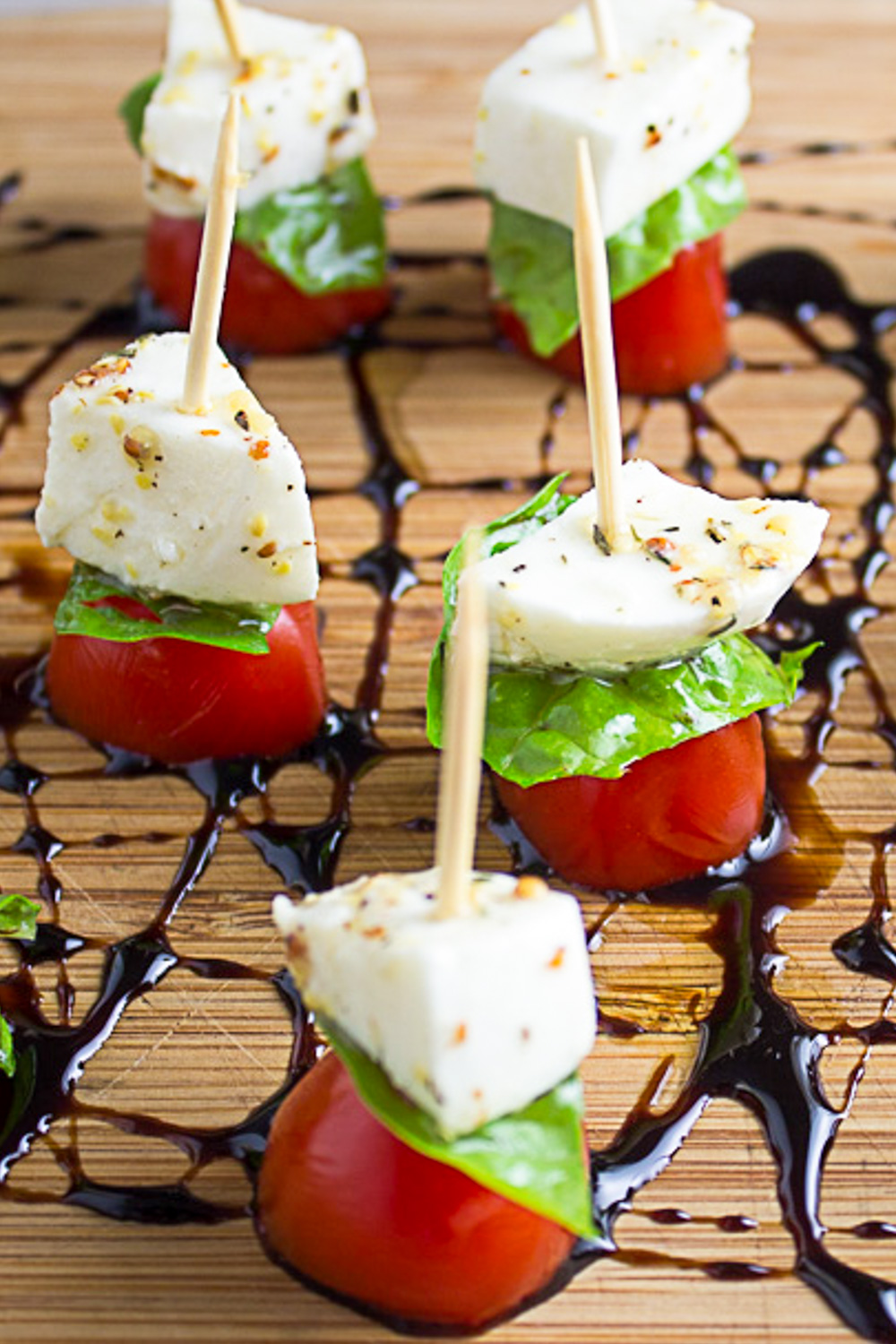 caprese salad on toothpicks placed on balsamic glaze drizzled on cutting board