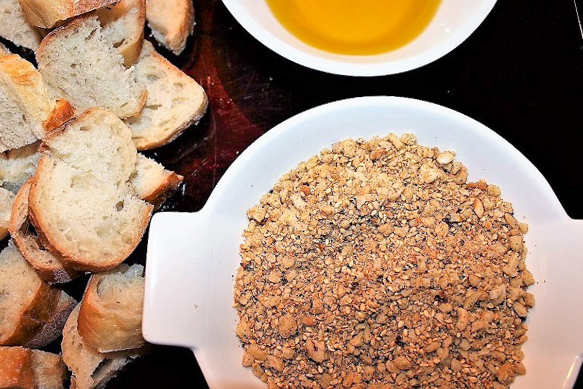 dukkah in bowl beside cut up baguette and olive oil