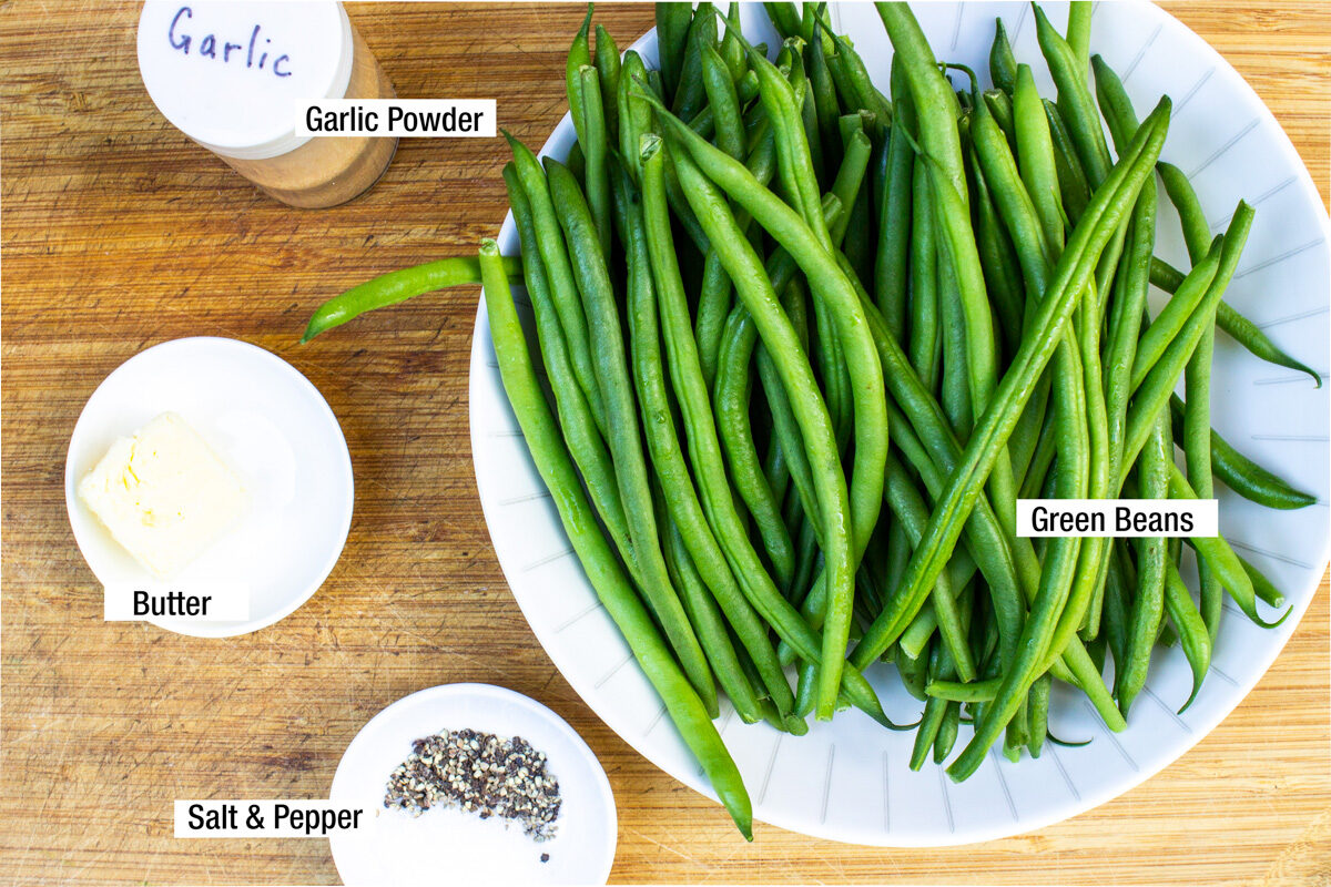 raw green beans in bowl, salt and pepper, butter, garlic powder on board