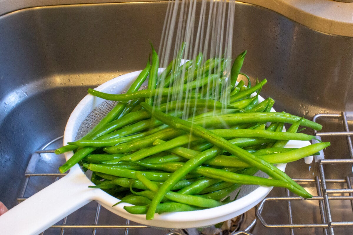 Water spraying on beans in colander over sink.