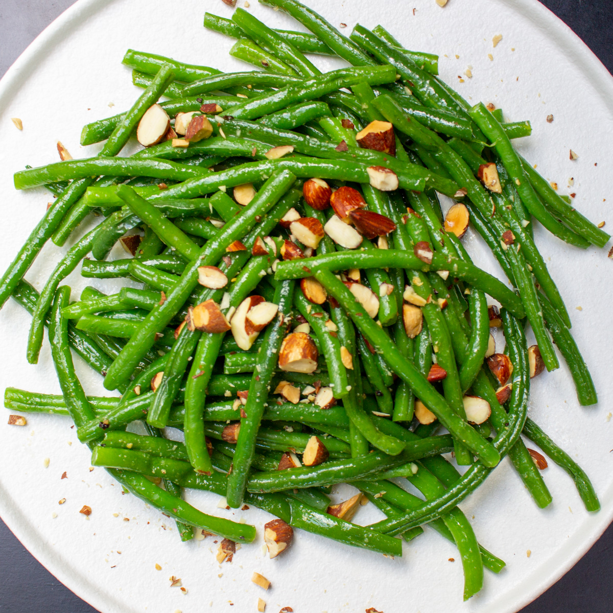 top view of green beans on white plate with chopped almonds on top