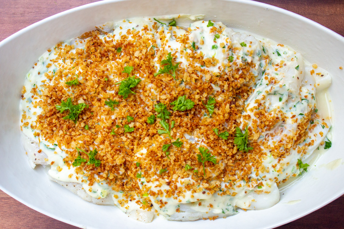 cooked cod topped with white sauce and panko crumbs in casserole dish