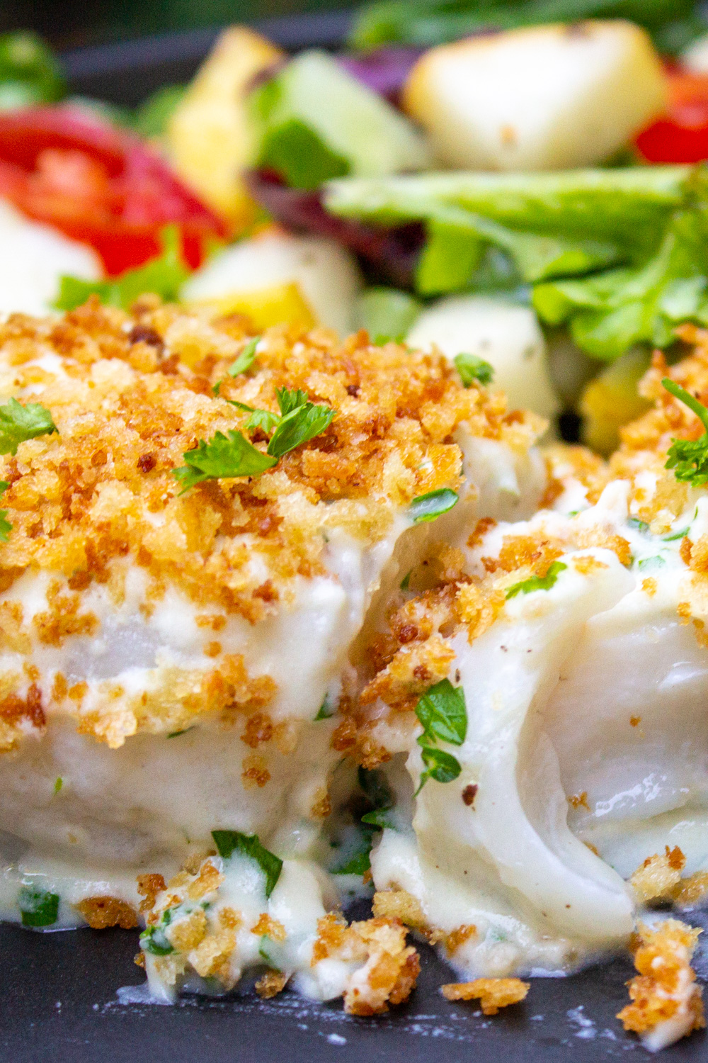 cod in bechamel sauce topped with panko with salad behind it  on plate