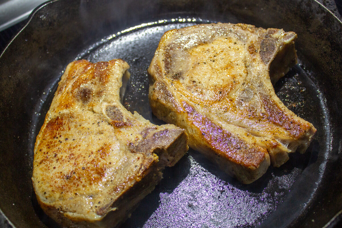 2 pork chops searing in cast iron pan