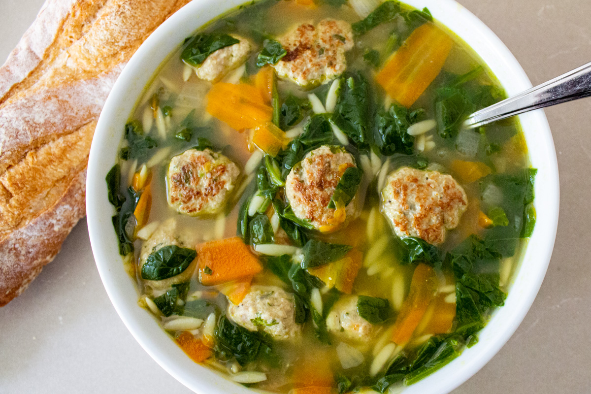 bowl of wedding soup with baguette beside it