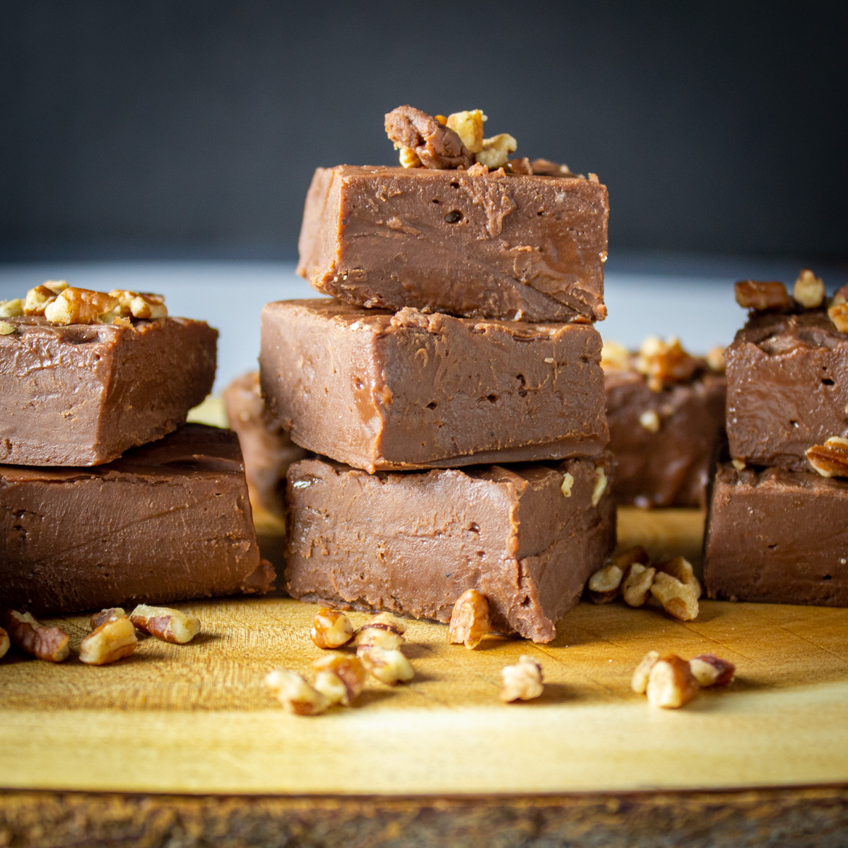 stacked squares of chocolate fudge with pecans on wooden tray.