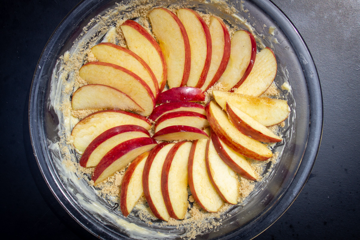 sliced apples fanned out on top of sugar and butter in pie plate