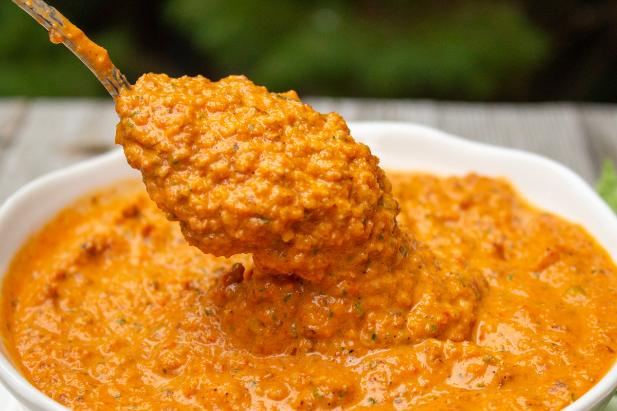 spoonful of red pepper sauce over bowl of red pepper sauce.
