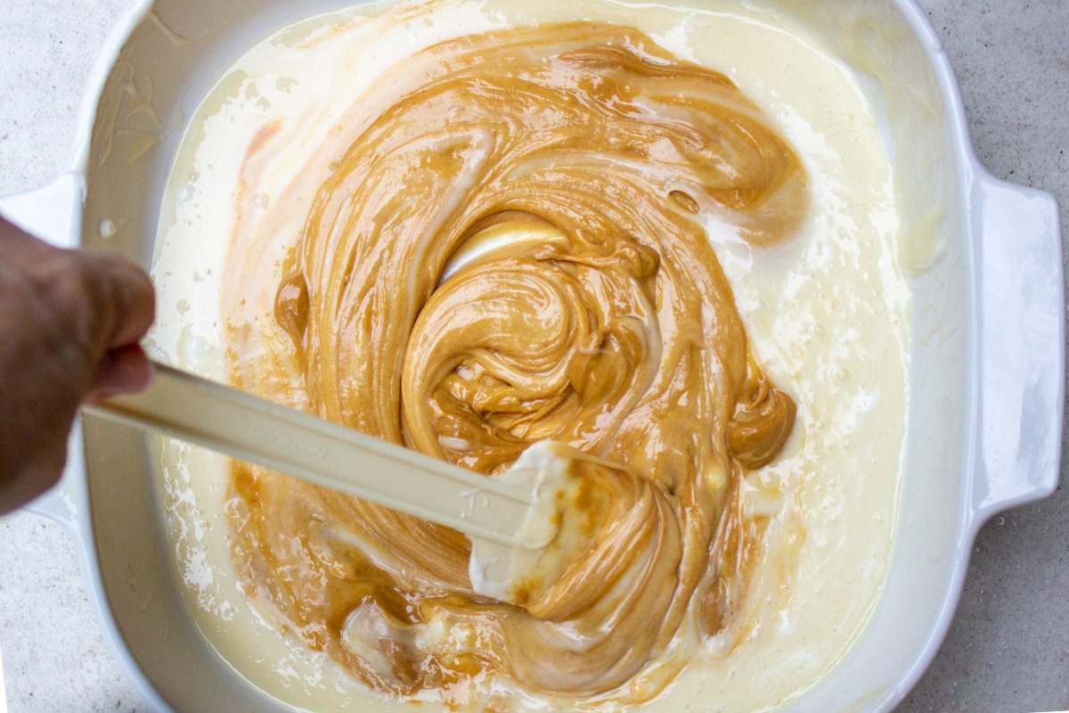 peanut butter being stirred into marshmallow mixture in pan