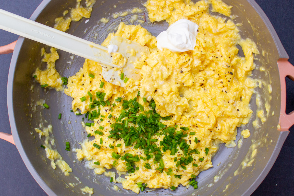 chives and sour cream added to scrambled eggs in skillet