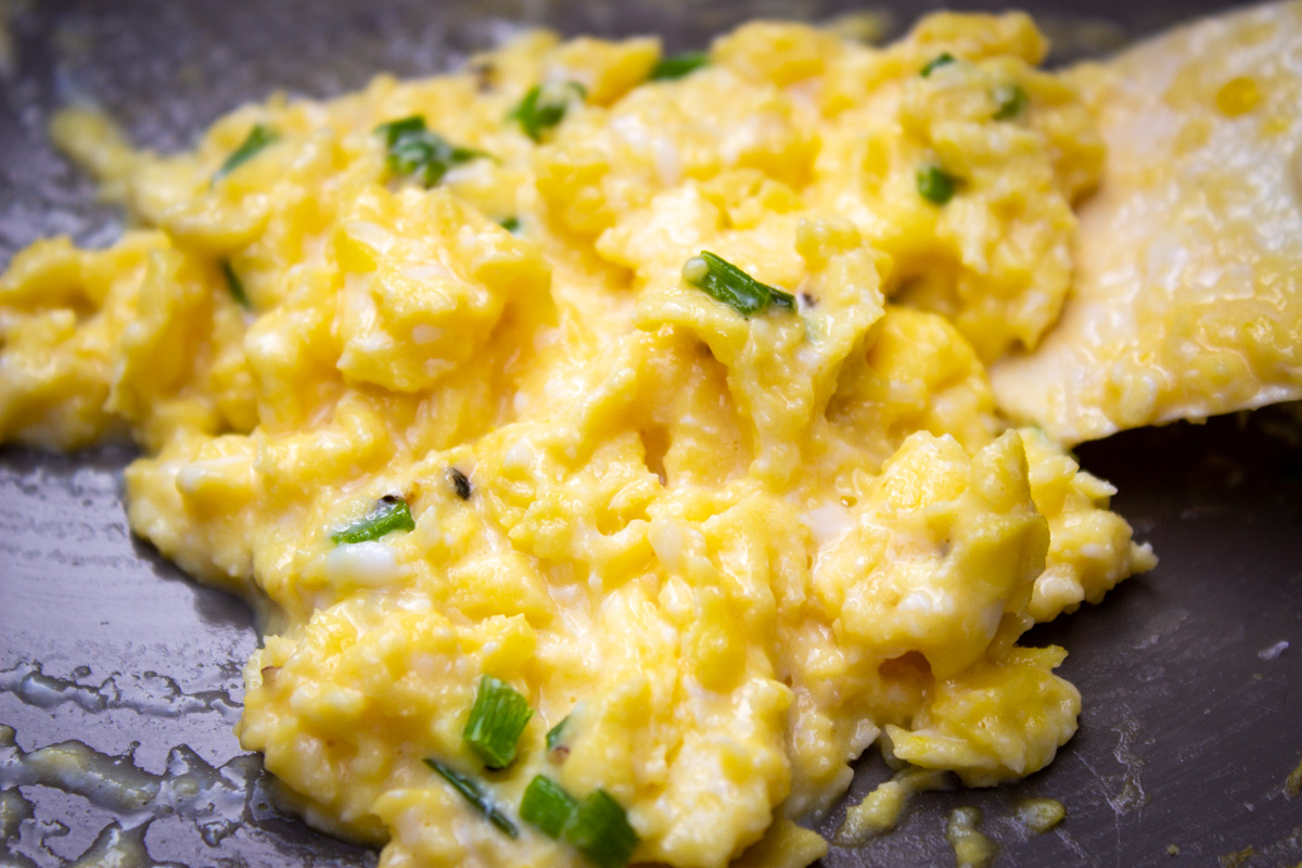 creamy scrambled eggs with chives in pan.