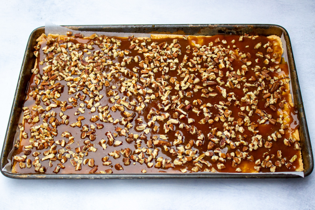 nuts sprinkled on crackers and toffee mixture in pan