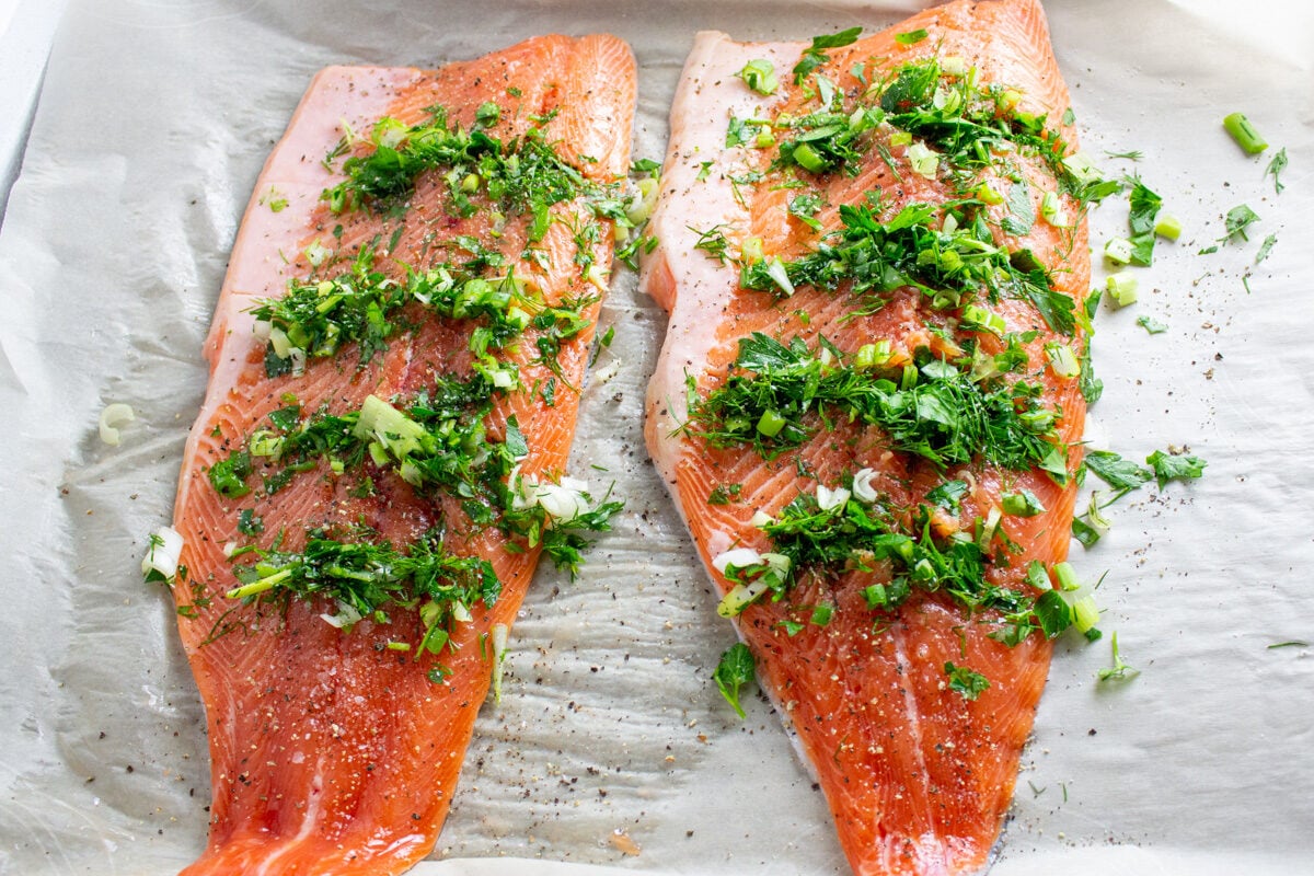 2 trout fillets stuffed with herb mixtures on parchment on pan before baking.