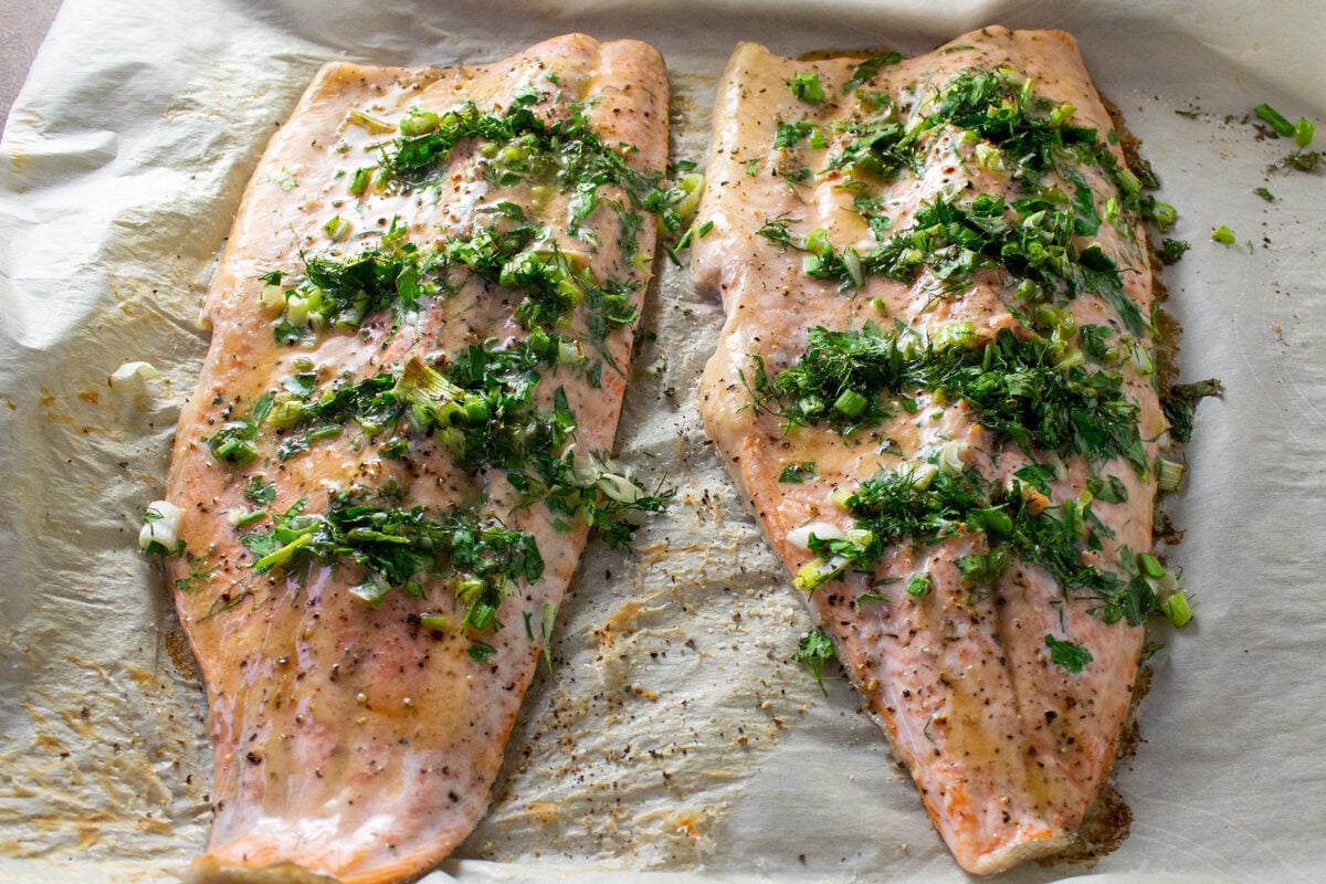 2 trout fillets stuffed with herb mixtures on parchment on pan after baking