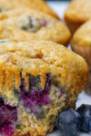 one banana blueberry muffin on table with fresh blueberries