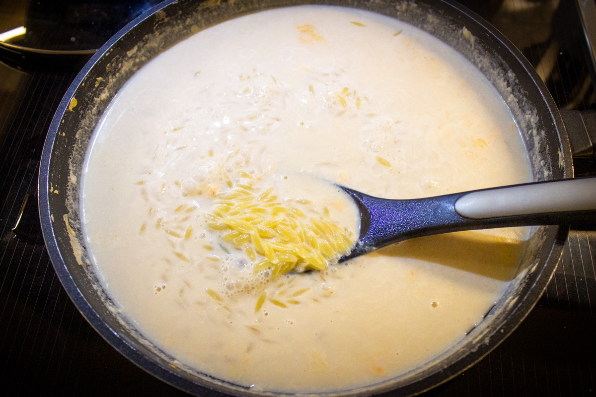 milk, broth and orzo boiling in skillet