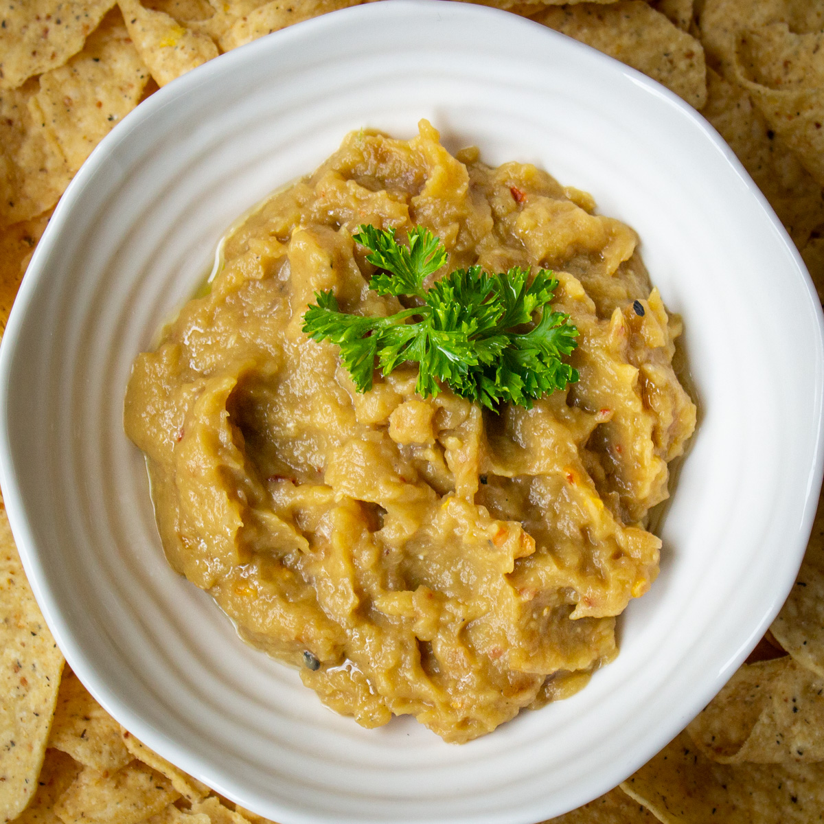 eggplant dip in white bowl with corn chips.