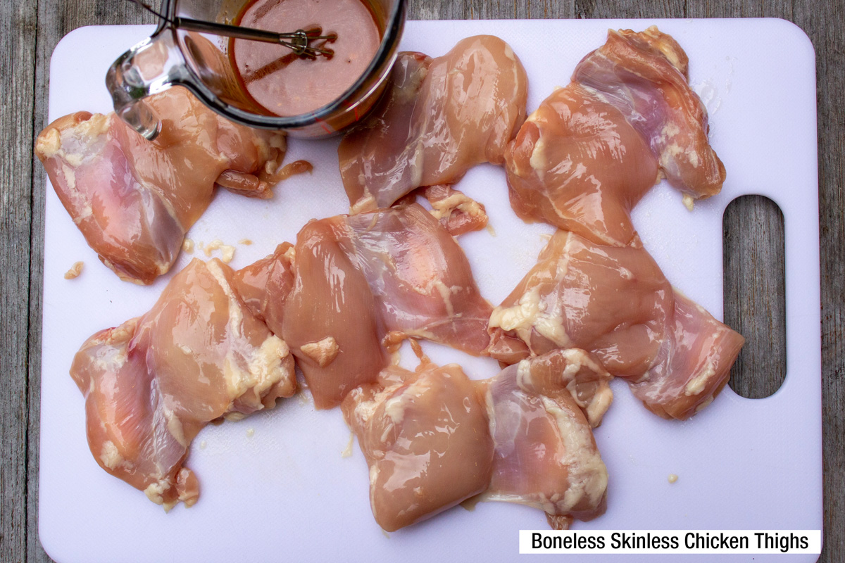 boneless skinless chicken thighs flattened on cutting board with sauce in cup