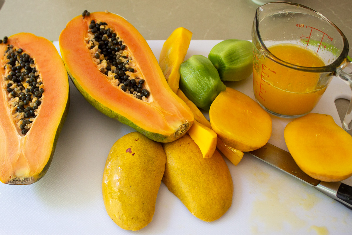 partially cut papaya and orange juice mango, peeled kiwi on cutting board.