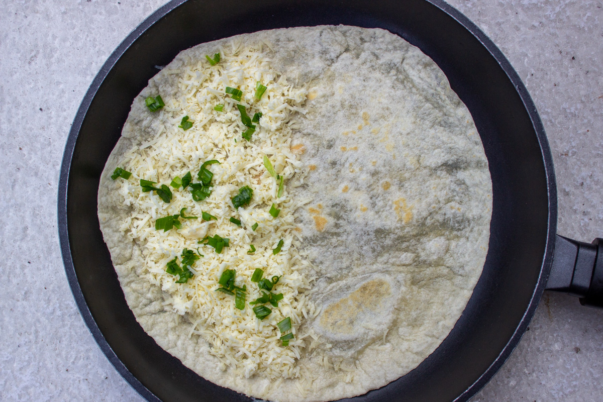 tortilla with cheese and green onion on skillet