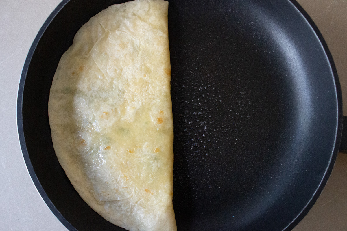 tortilla with cheese folded in half on skillet.