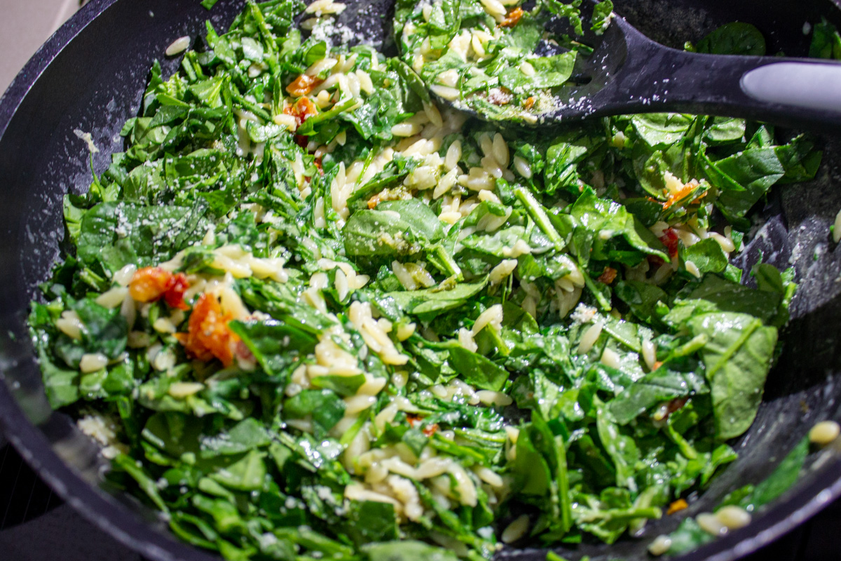 fresh spinach added to cooked orzo and parmesan sauce in pan
