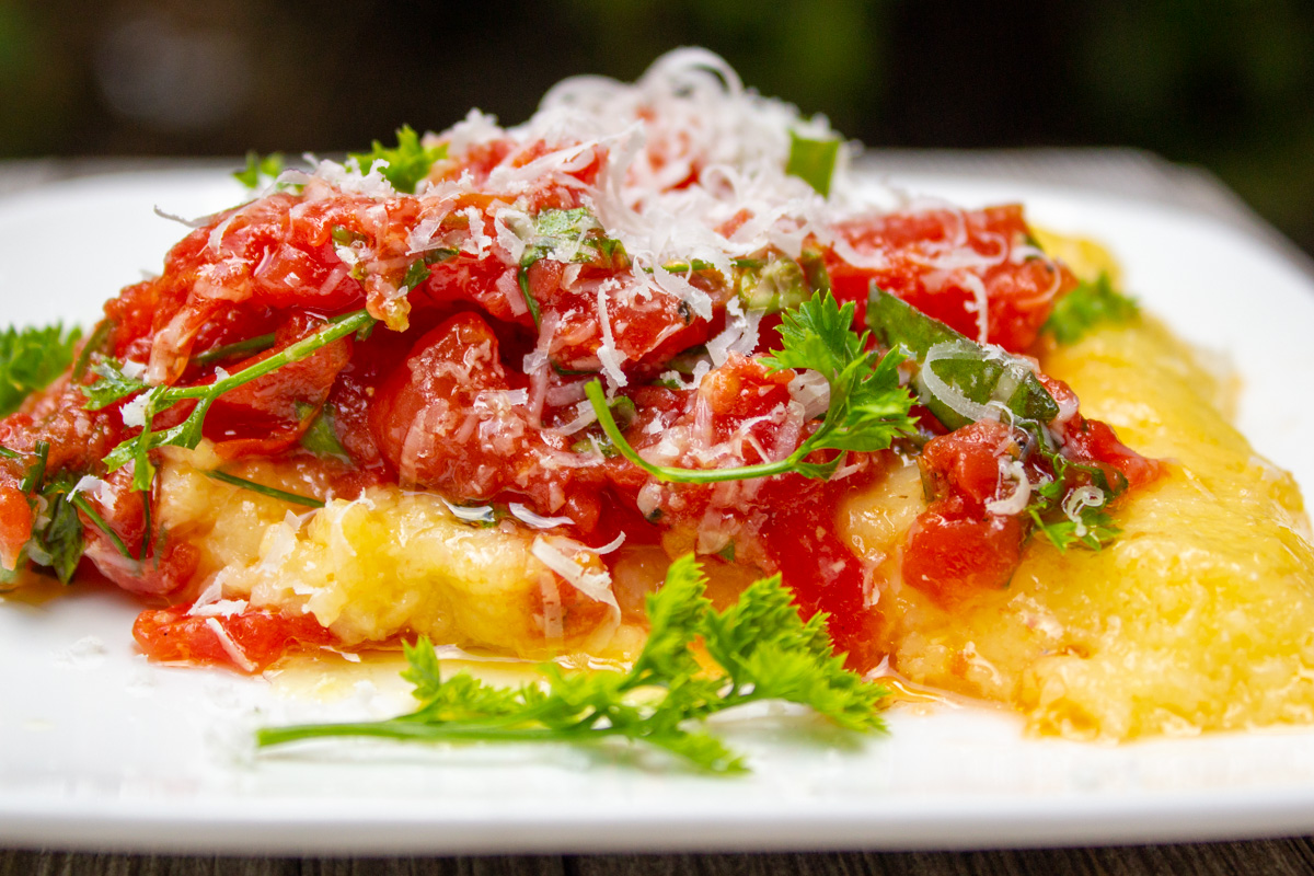 plate of polenta covered with tomato salad and parmesan.