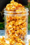 salted caramel popcorn in a tall clear jar on table.