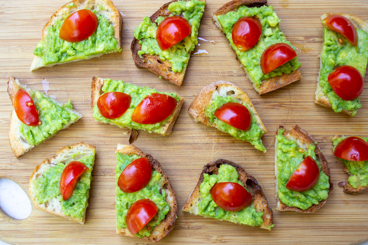 crostini with avocado topped with tomato on cutting board.