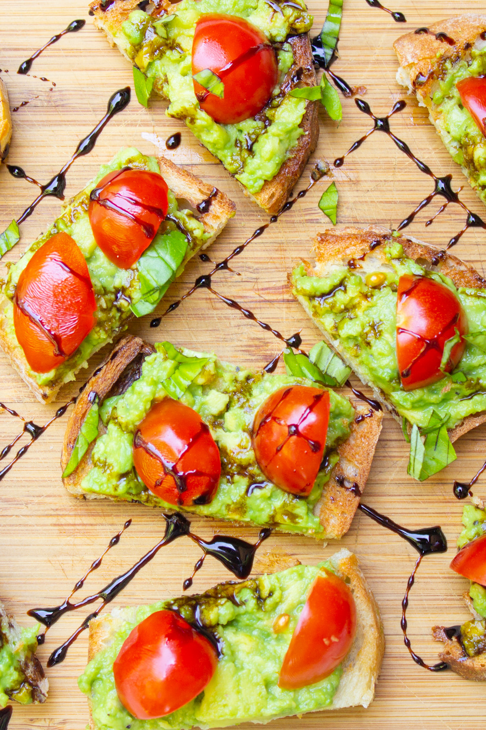 avocado and tomatoes on crostini with balsamic drizzle on cutting board