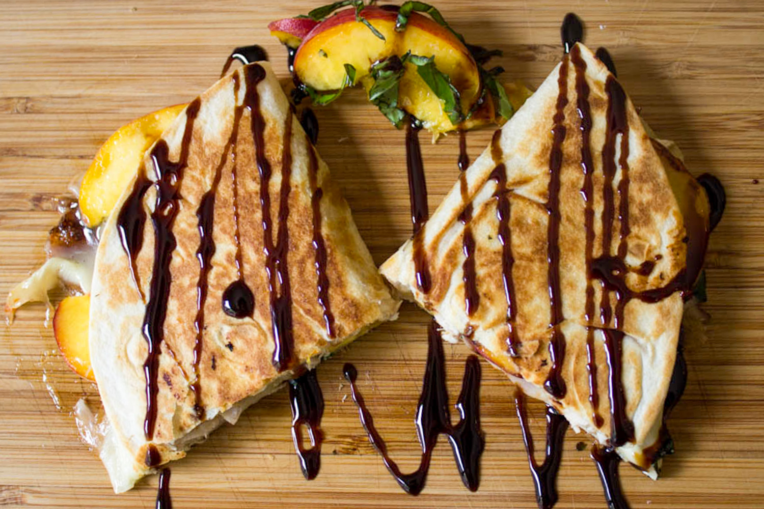 two chicken quesadilla wedges on cutting board drizzled with balsamic reduction.