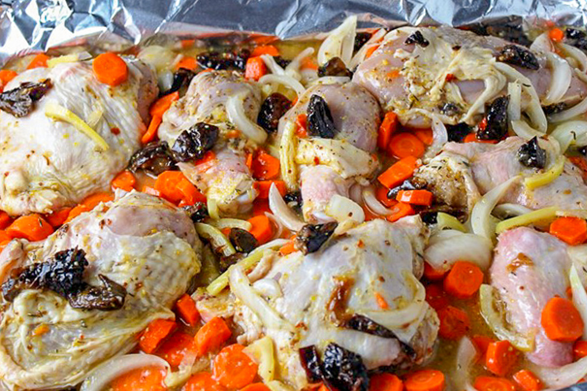company chicken pieces with veggies citrus and fruit in pan before baking.