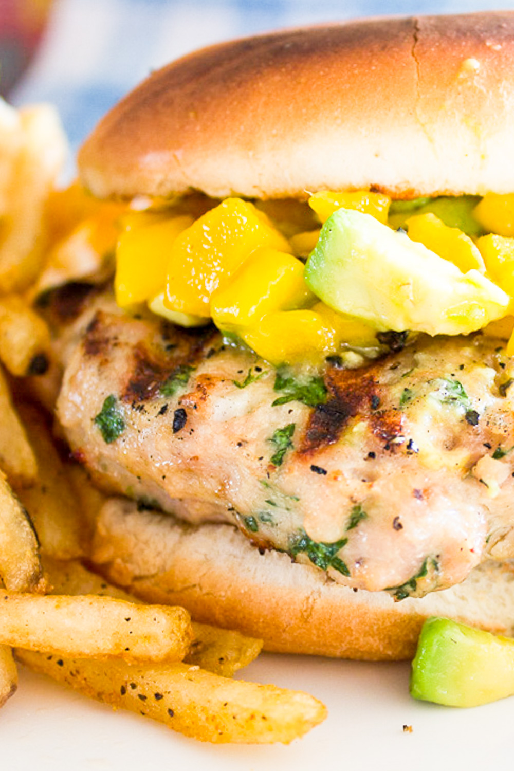 grilled chicken burger with mango salsa with fries on plate.