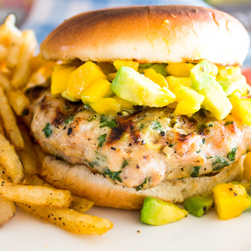 grilled chicken burger with mango salsa with fries on plate.