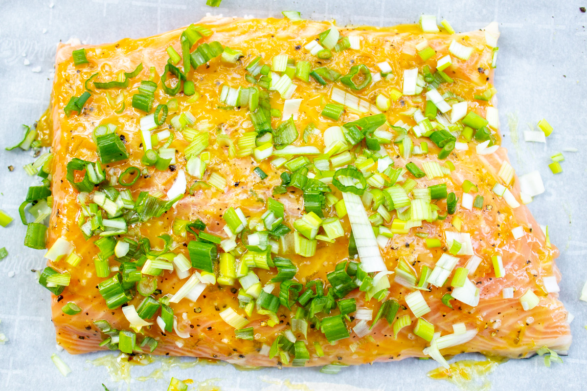 uncooked salmon fillet with citrus glaze and chopped green onions on pan.