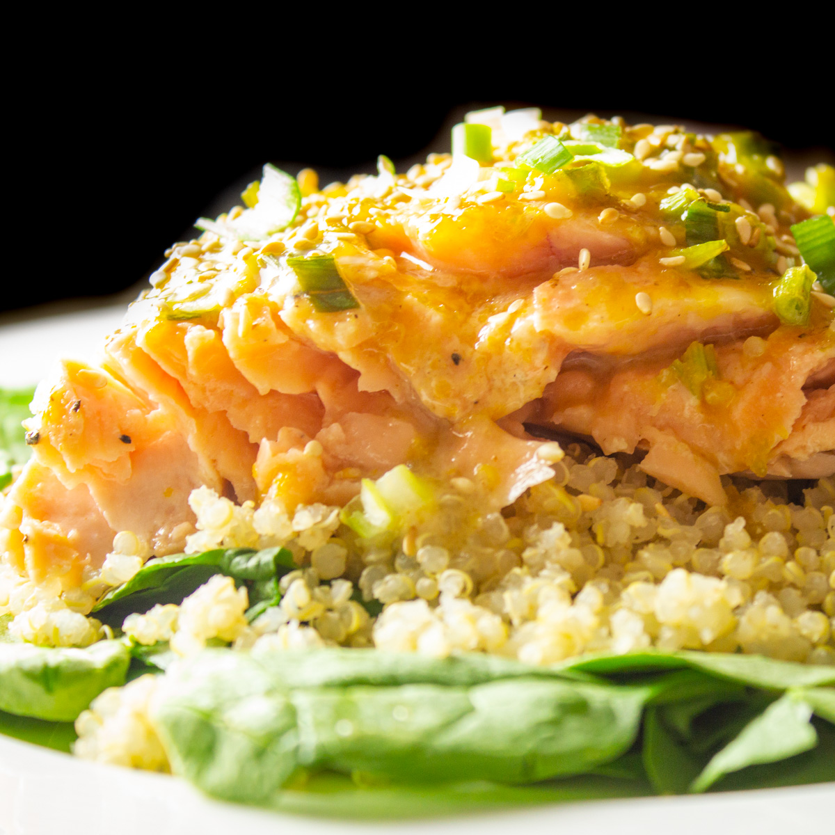 salmon with citrus glaze on top of quinoa and spinach on plate.