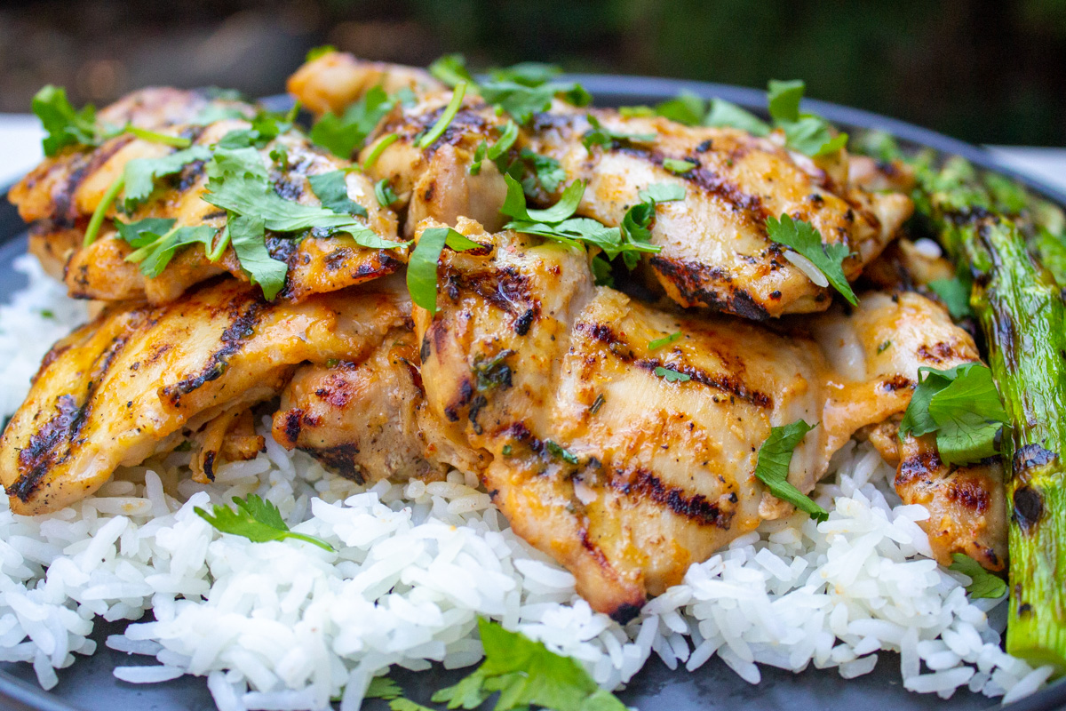 grilled boneless chicken thighs over rice on plate sprinkled with cilantro.