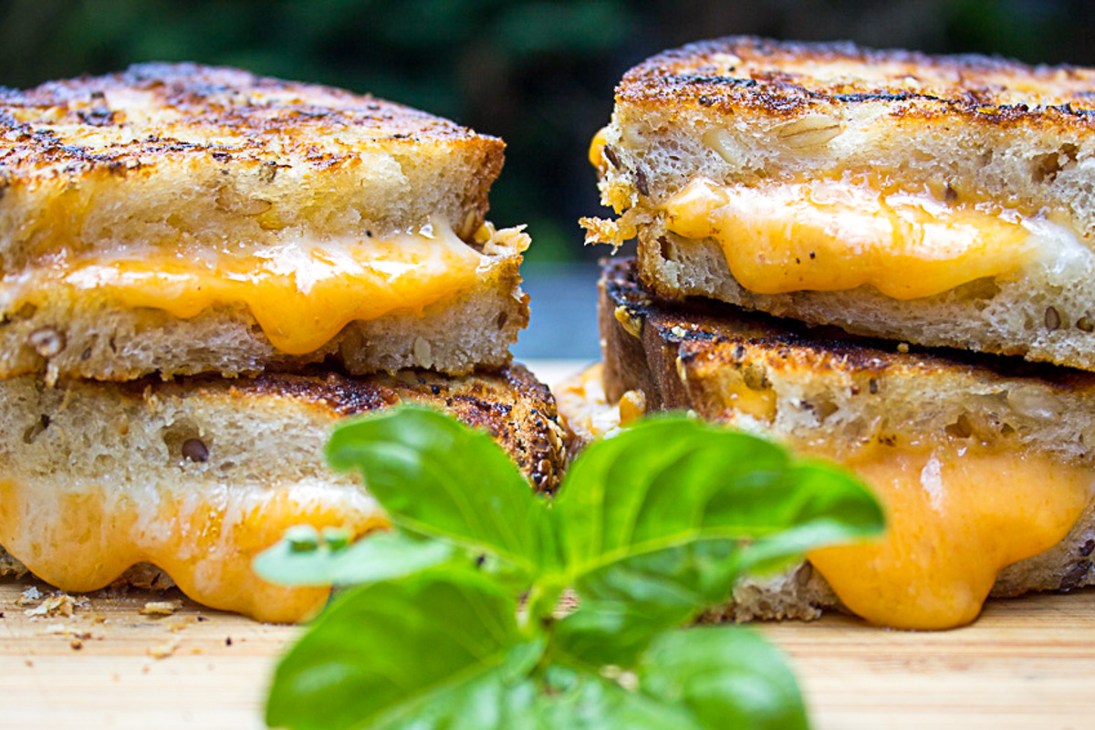 two oozing stacked grilled cheese sandwiches on cutting board.