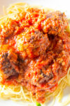 Italian meatballs in marinara sauce over spaghetti in bowl.