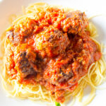 Italian meatballs in marinara sauce over spaghetti in bowl.