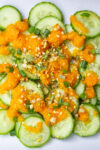Japanese ginger salad dressing drizzled on sliced cucumbers garnished with sesame seeds and green onions.