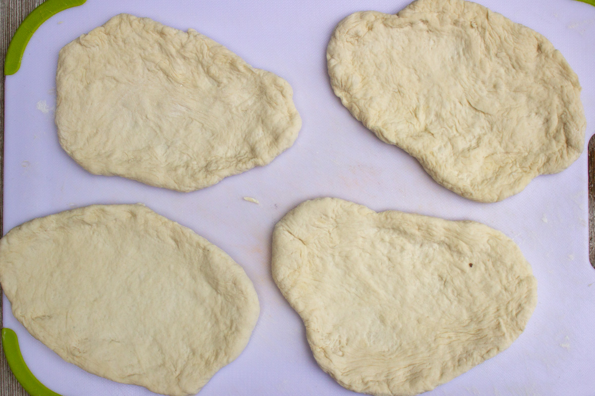 4 pieces of dough stretched out on cutting board in shape of naan.