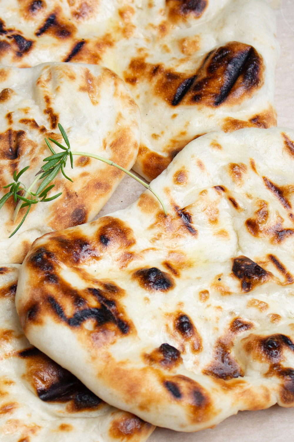 pile of 4 grilled naan on cutting board.