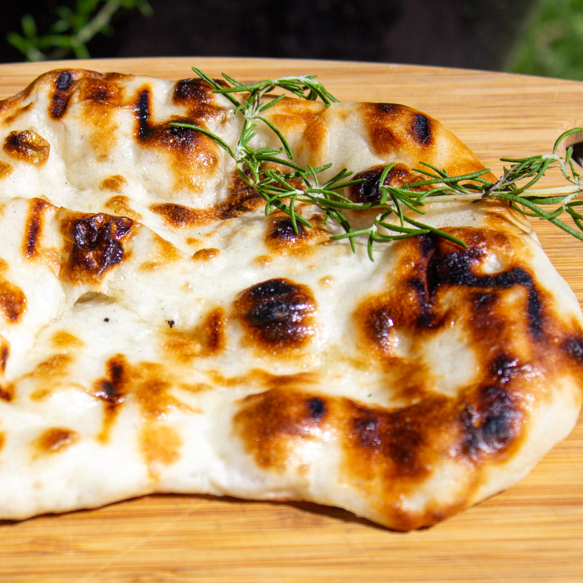 one brown puckered naan with sprig of rosemary on cutting board.