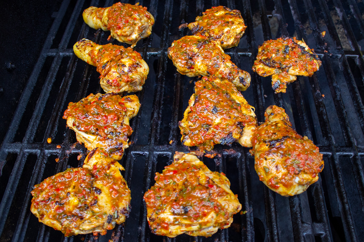 extra sauce brushed on peri peri chicken while cooking on grill.