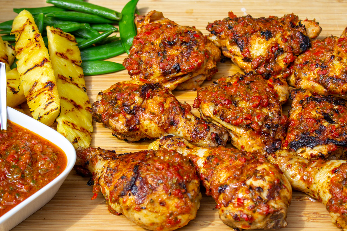 finished peri peri chicken on cutting board with pineapple spears, peas and extra peri peri sauce.