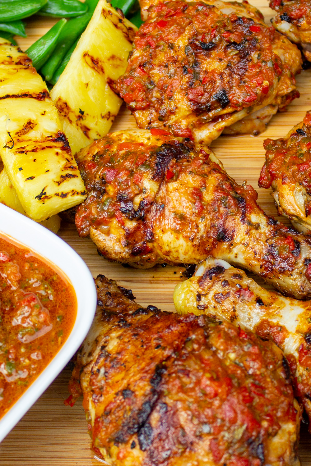 finished peri peri chicken on cutting board with pineapple spears, peas and extra peri peri sauce.