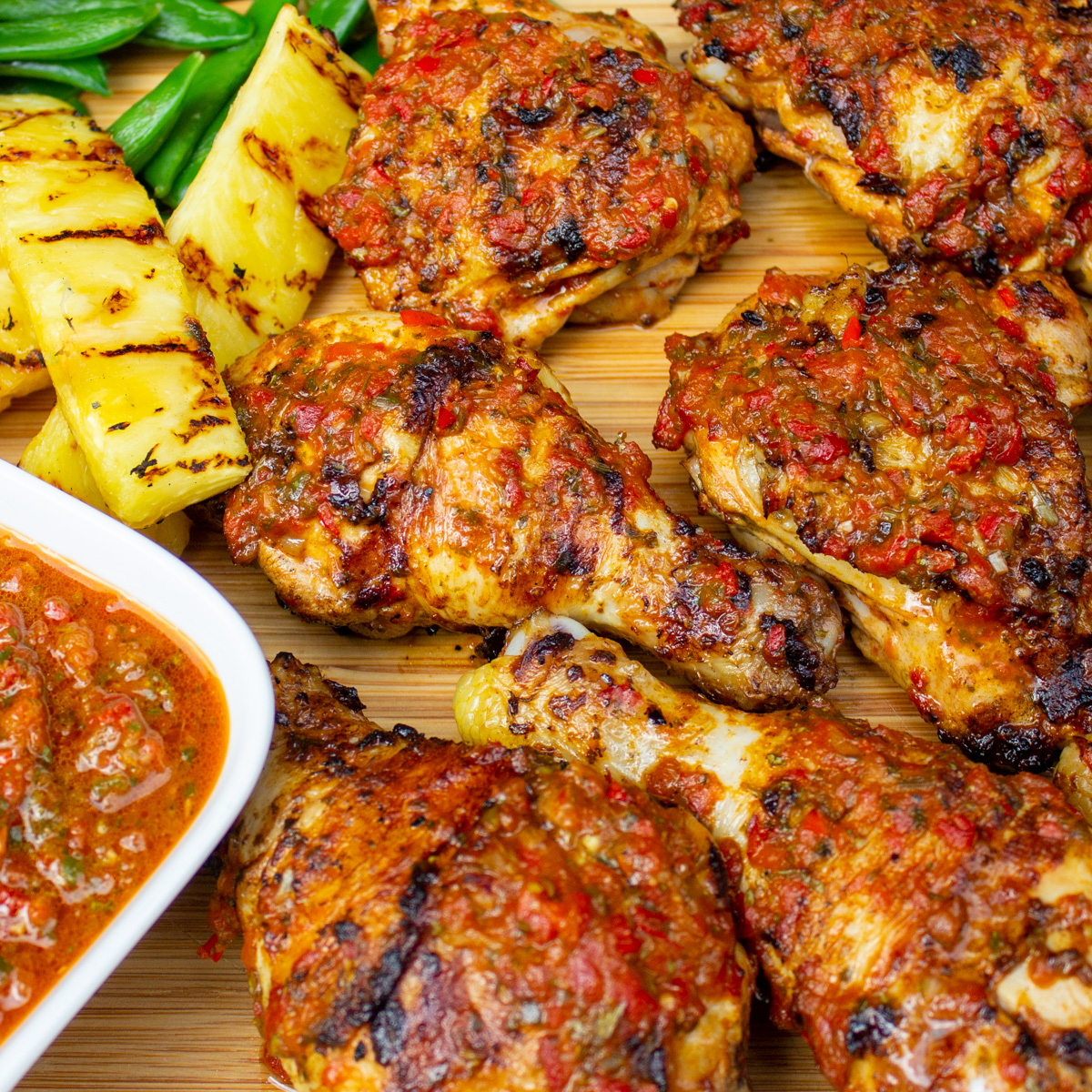 finished peri peri chicken on cutting board with pineapple spears, peas and extra peri peri sauce.